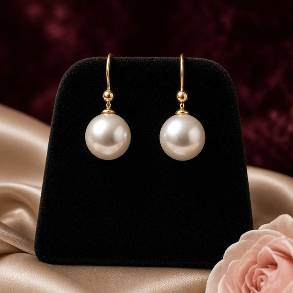 Moonlit Pearl Drop Earrings – White pearl drop earrings on gold hooks on a black velvet stand with champagne satin and blush roses (product image, invented unbranded)